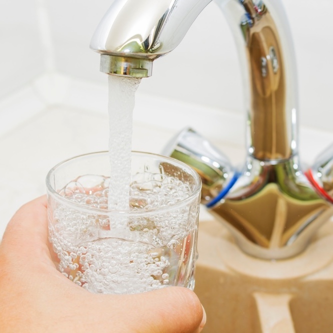 Water from a faucet is flowing into the glass.